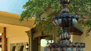 Una fuente con un borde de mosaico, la entrada de un edificio y pavimento de baldosas.