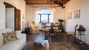 Un salon chaleureux avec un plafond en bois, un canapé blanc, une table à manger avec des chaises et une vue dégagée sur l’extérieur grâce à une grande fenêtre.
