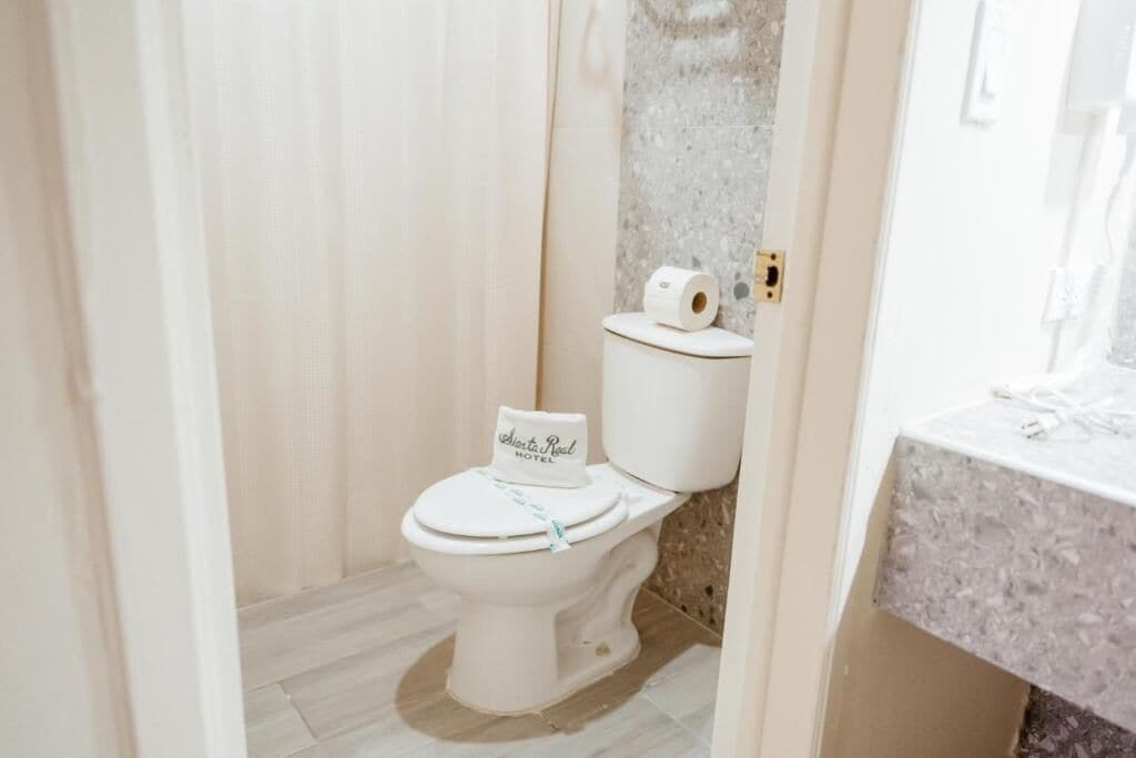 Inodoro blanco con un letrero en la tapa, pared de mármol y encimera de baño.