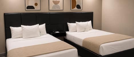 Habitación de hotel con dos camas, cabecero negro, ropa de cama blanca y tres obras de arte enmarcadas en la pared.