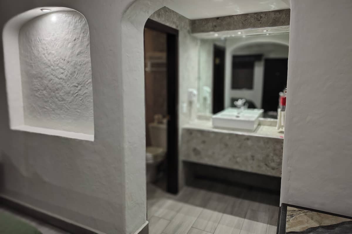 Un baño moderno con encimera de mármol, un espejo y una luz empotrada en el techo.