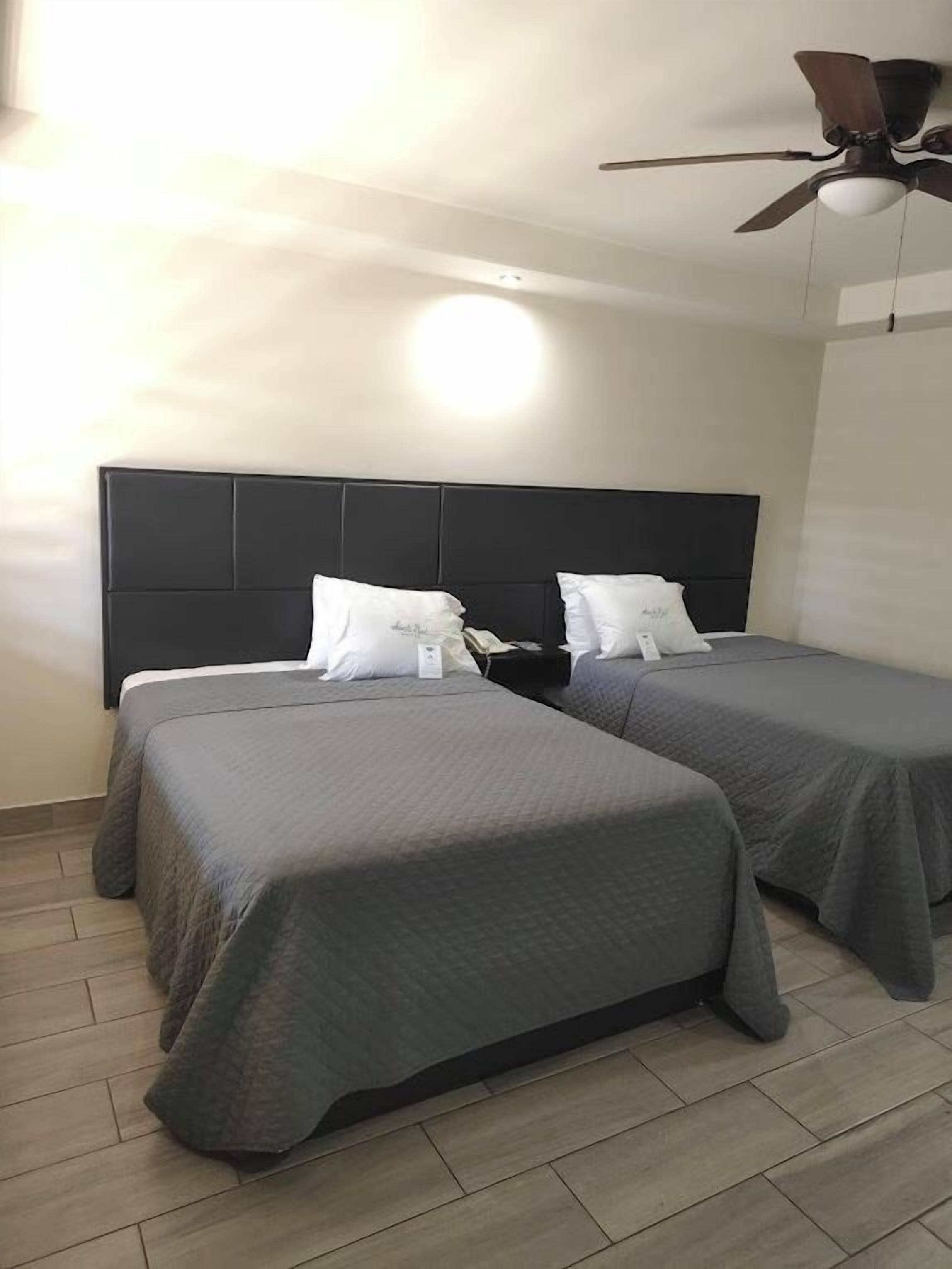 A hotel room with two beds, a ceiling fan, and a light fixture.