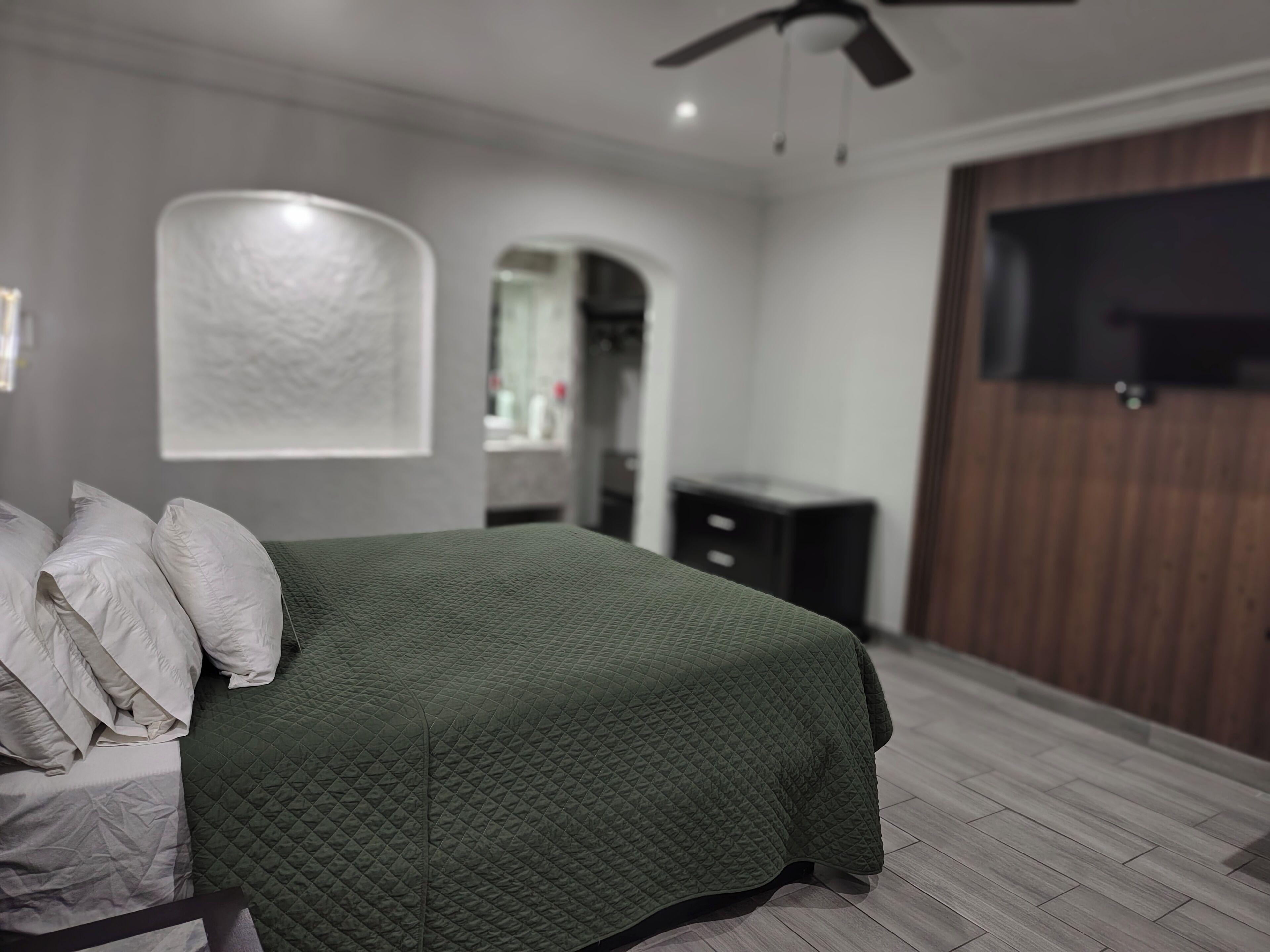 A bedroom with a bed, a ceiling fan, a TV, and a wooden wardrobe.