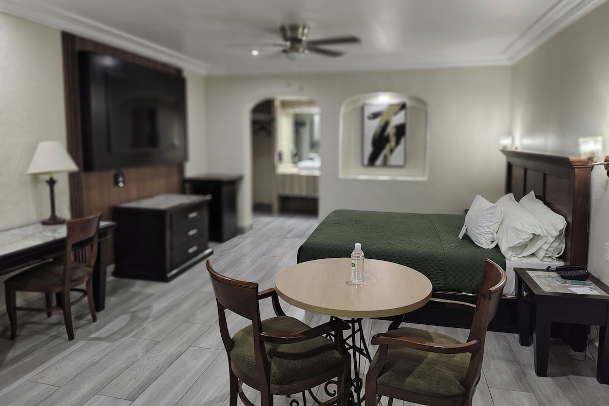 Una habitación de hotel con cama, escritorio, silla, televisor y ventilador de techo.