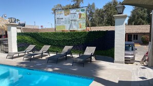 A poolside area with lounge chairs and a menu board in the background. - Hotel Siesta Real (Mexicali)