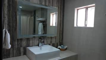 A bathroom with a large mirror, a white sink, a shower area, and a window.