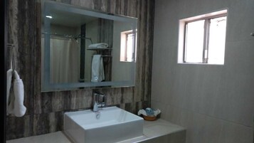 A bathroom with a large mirror, a white sink, a shower area, and a window.
