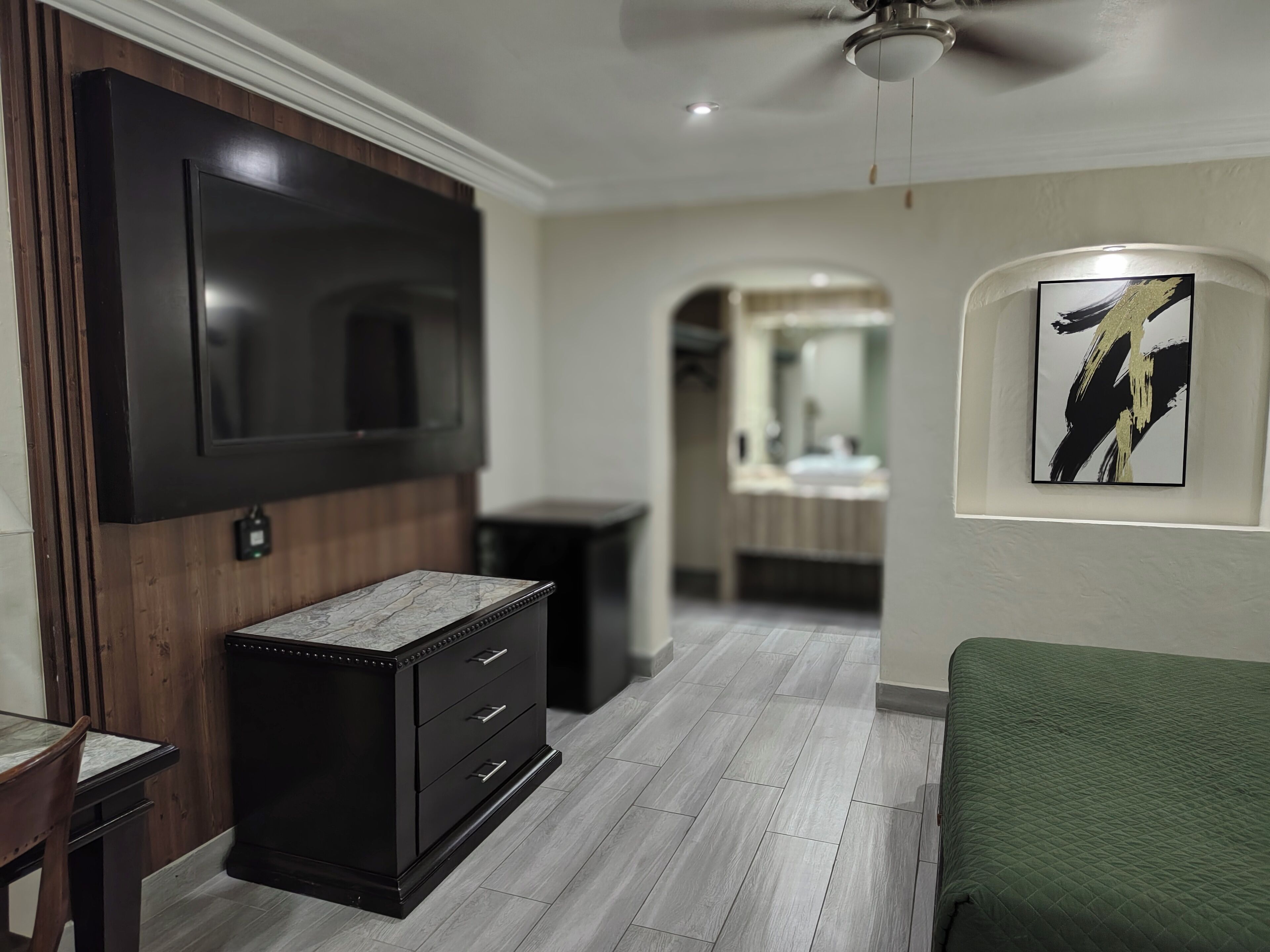 A modern living room with a flat-screen TV, a marble-top cabinet, a green armchair, and a framed artwork on the wall.