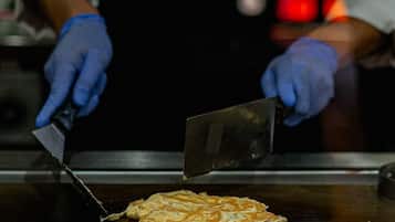 Una persona con guantes usando un machete grande para cortar algo de comida sobre una superficie de cocina plana.
