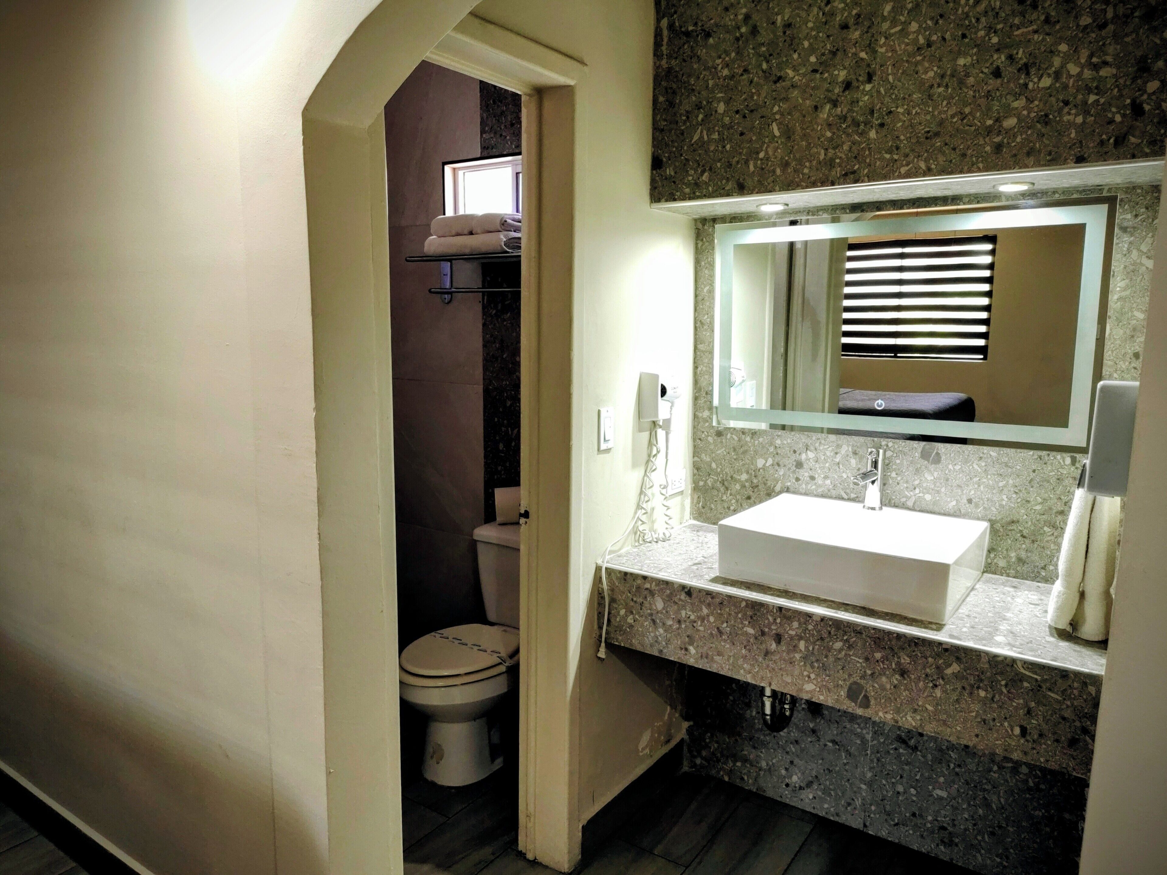 A bathroom with a white sink, a mirror above it, and a toilet visible through an open doorway.