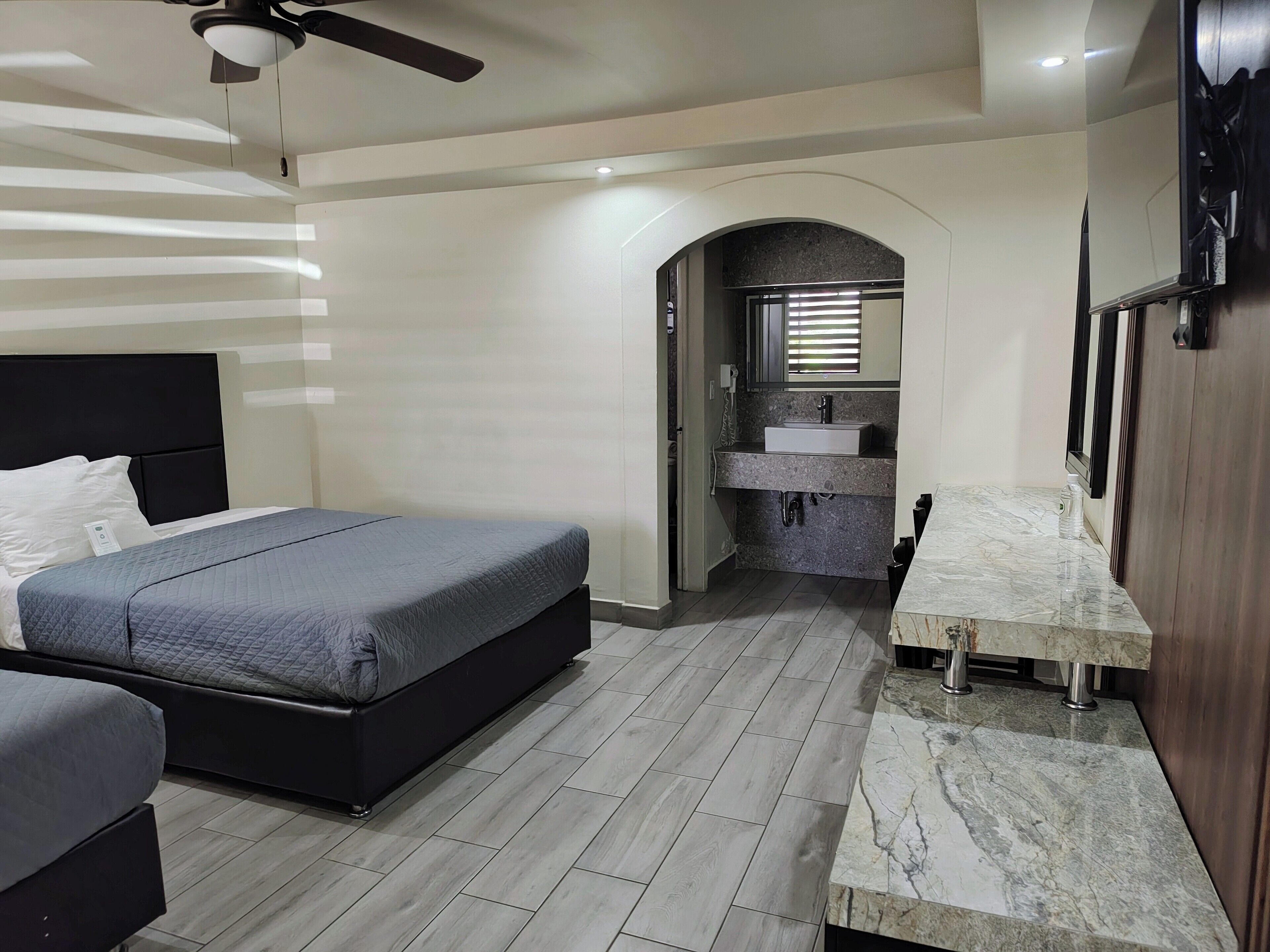 Quarto moderno com cama, escrivaninha e banheiro com pia e espelho.