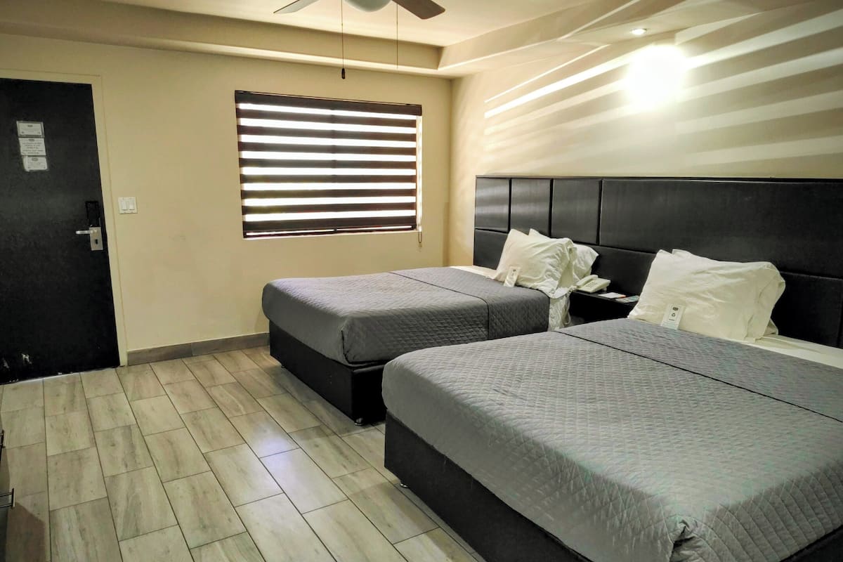 Habitación de hotel con dos camas, un ventilador de techo, una ventana con persianas y una puerta.