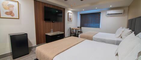 A hotel room with two beds, a television, a ceiling fan, an air conditioning unit, and a small table with chairs.
