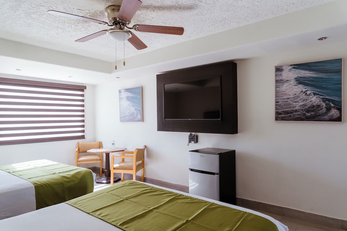 Habitación de hotel con dos camas, un escritorio, una silla, un televisor y un ventilador de techo.