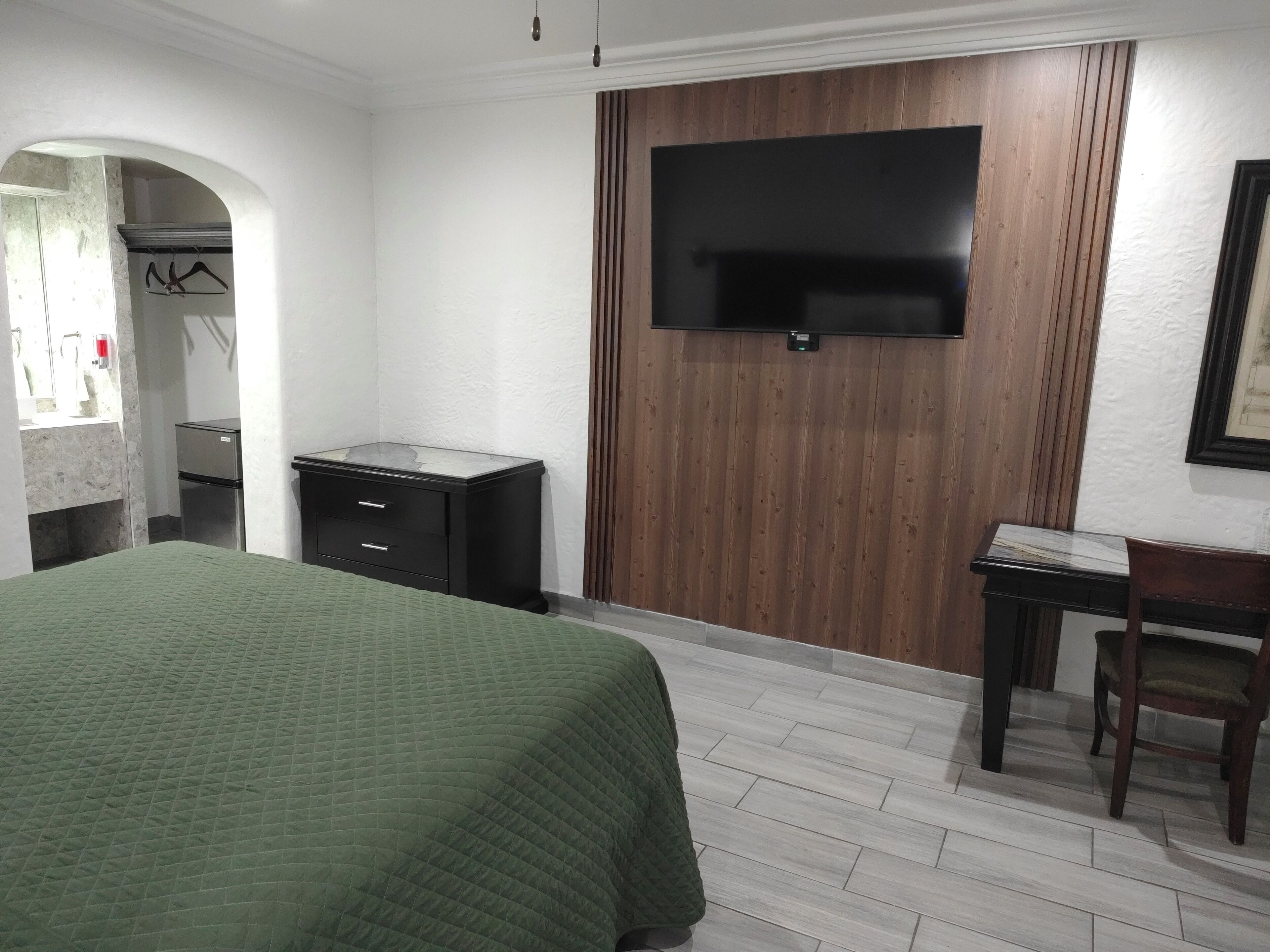 Habitació d'hotel amb llit, escriptori, televisió penjada a un panell de paret de fusta, armari i mirall.