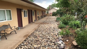 Un motel con una fila di stanze, un vialetto in cemento e un'area giardino con rocce e piante.