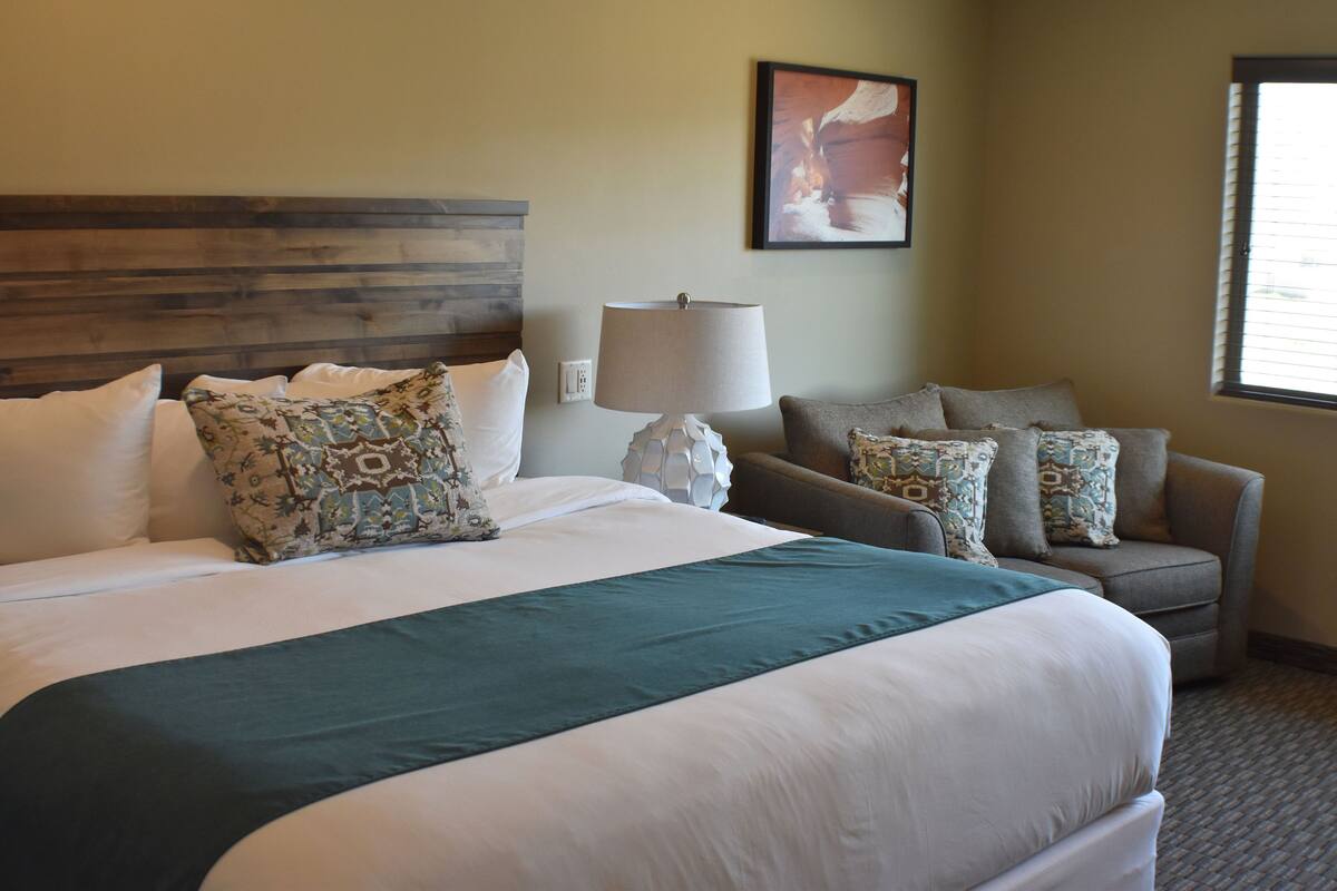 A hotel room with a large bed, a sofa, a lamp, and a painting on the wall.