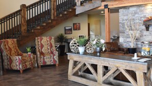 A spacious living area with a wooden staircase, a stone fireplace, and a central island with seating and decorative plants. - Canyon Country Lodge (Escalante)