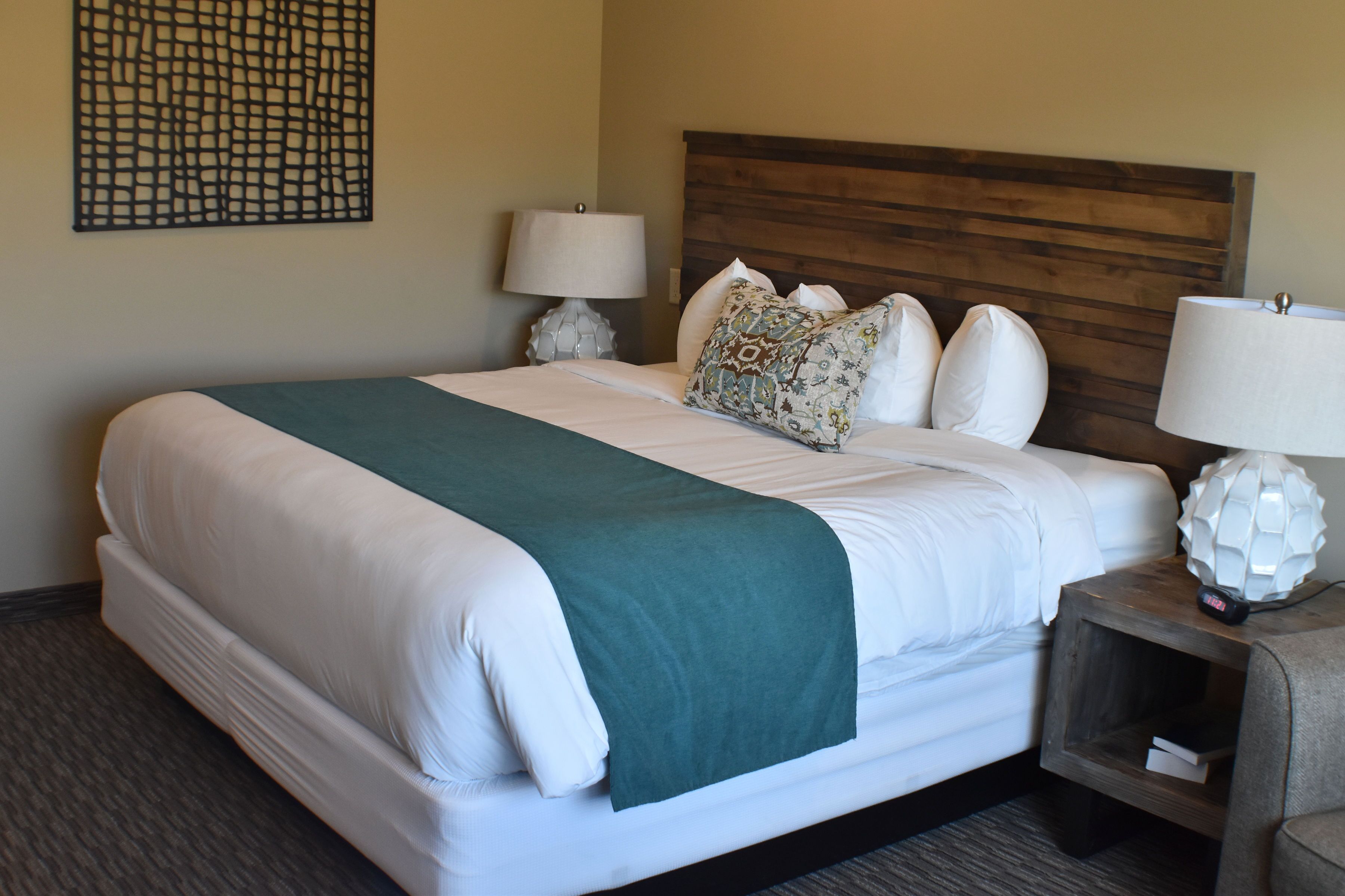 A neatly made bed with a green throw, white linens, and patterned pillows. There are two bedside tables with lamps and decorative items.