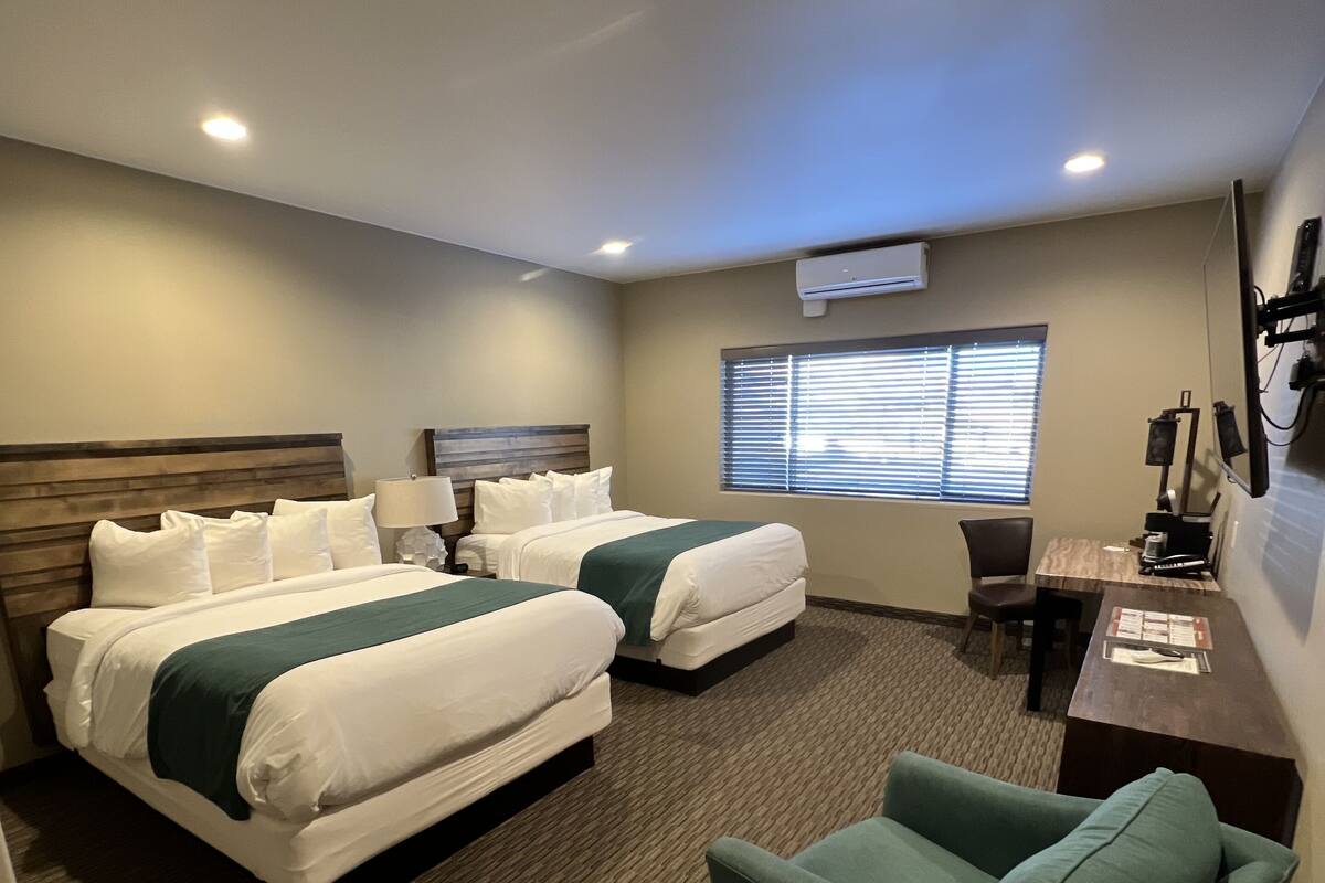 A hotel room with two beds, a desk, a chair, and a TV.