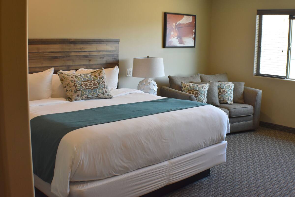 A hotel room with a large bed, a sofa, a lamp, and a painting on the wall.