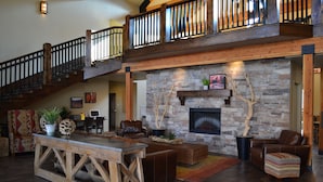A spacious living area with a stone fireplace, wooden staircase, and leather furniture. - Canyon Country Lodge (Escalante)