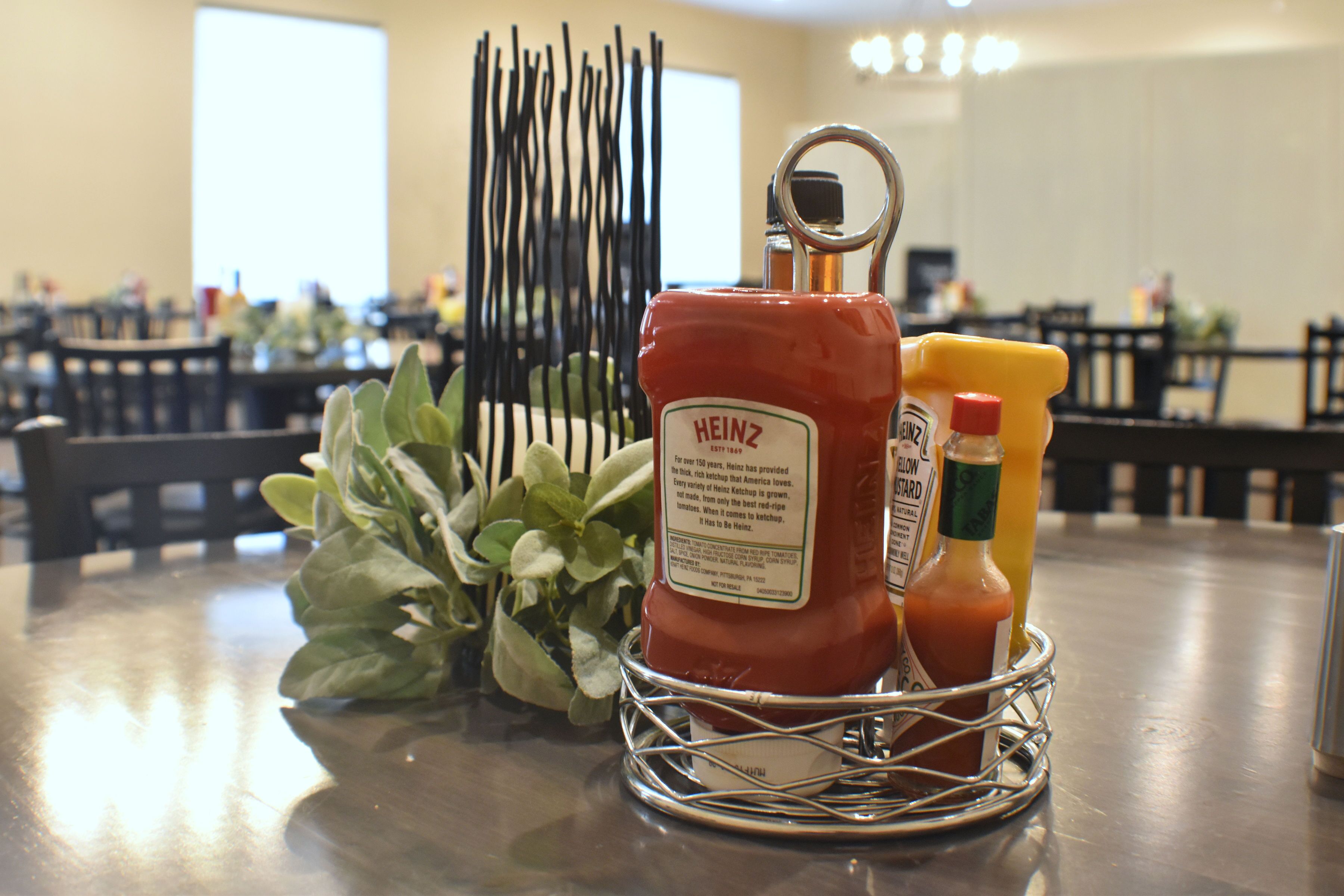 Une table sur laquelle se trouve un panier en métal contenant un flacon de ketchup Heinz, un flacon de moutarde et un flacon de moutarde jaune.