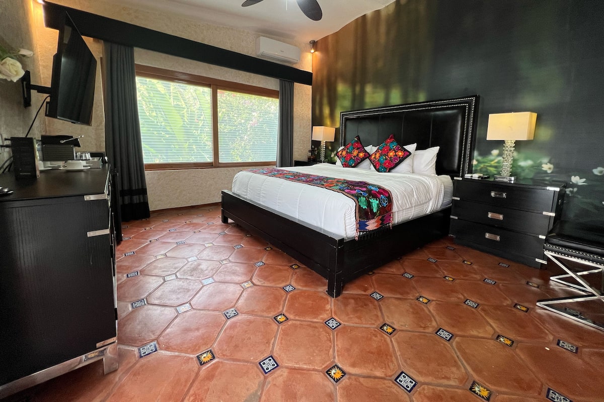 A bedroom with a bed, a desk, a TV, and a ceiling fan.