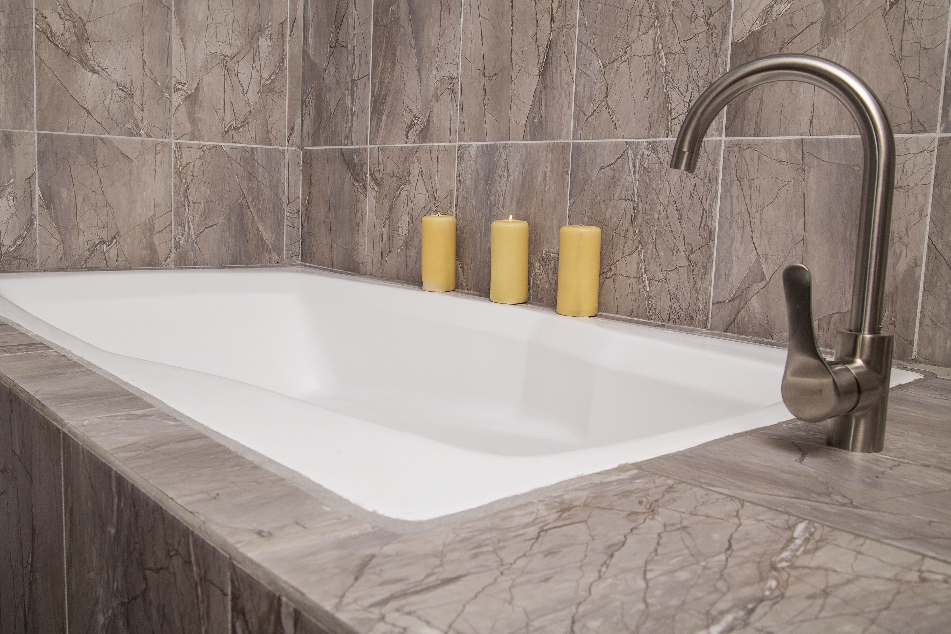Un baño con una bañera blanca grande, un grifo moderno y tres velas en la pared.