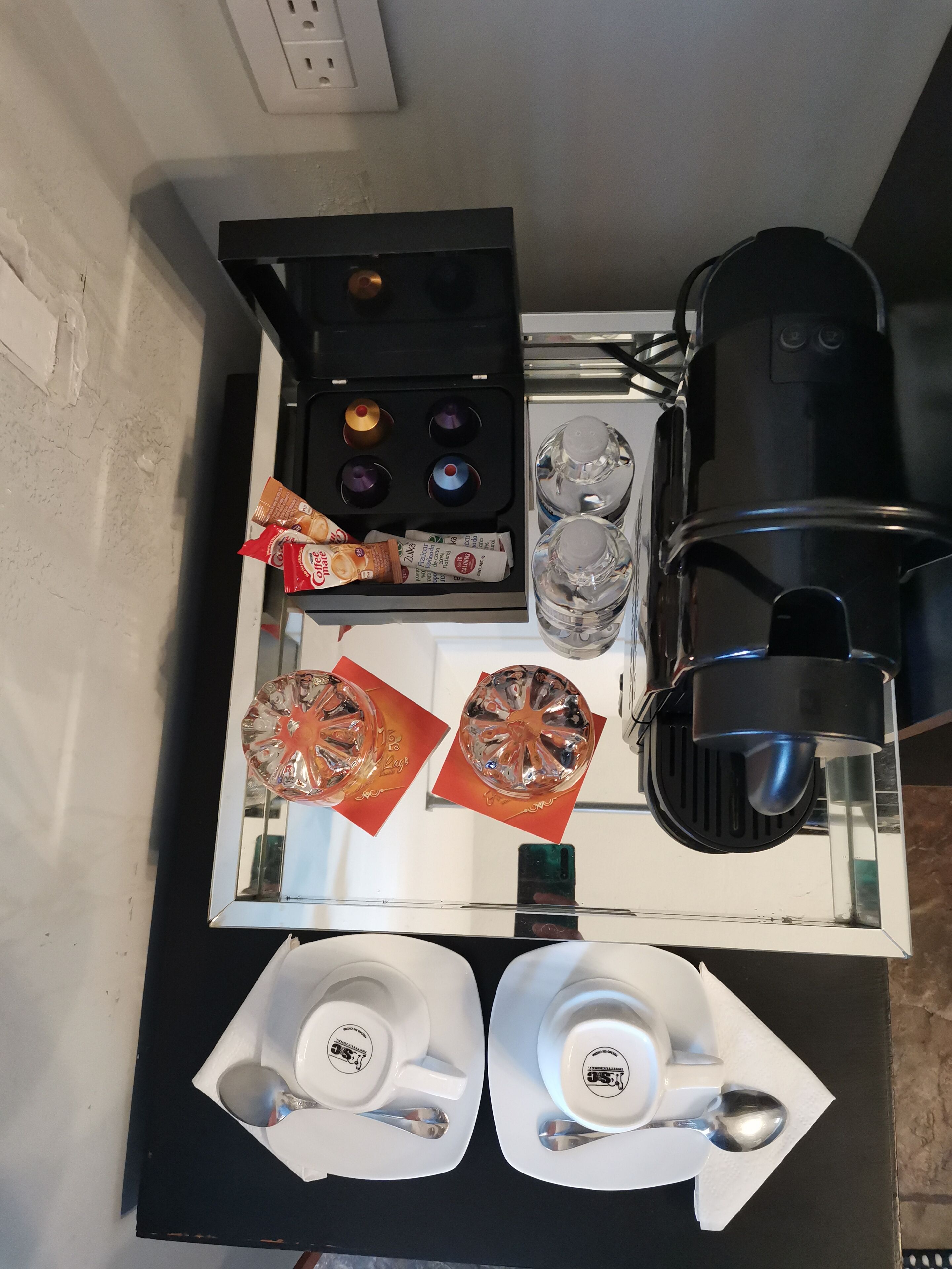Une petite cuisine équipée d’une machine à café, d’une bouilloire, d’un four à micro-ondes et d’un petit réfrigérateur. On trouve deux tasses et une cuillère sur le comptoir.