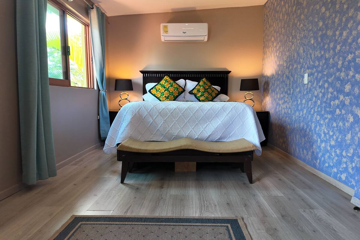 A bedroom with a bed, two bedside lamps, a wall-mounted air conditioner, and a patterned wall.