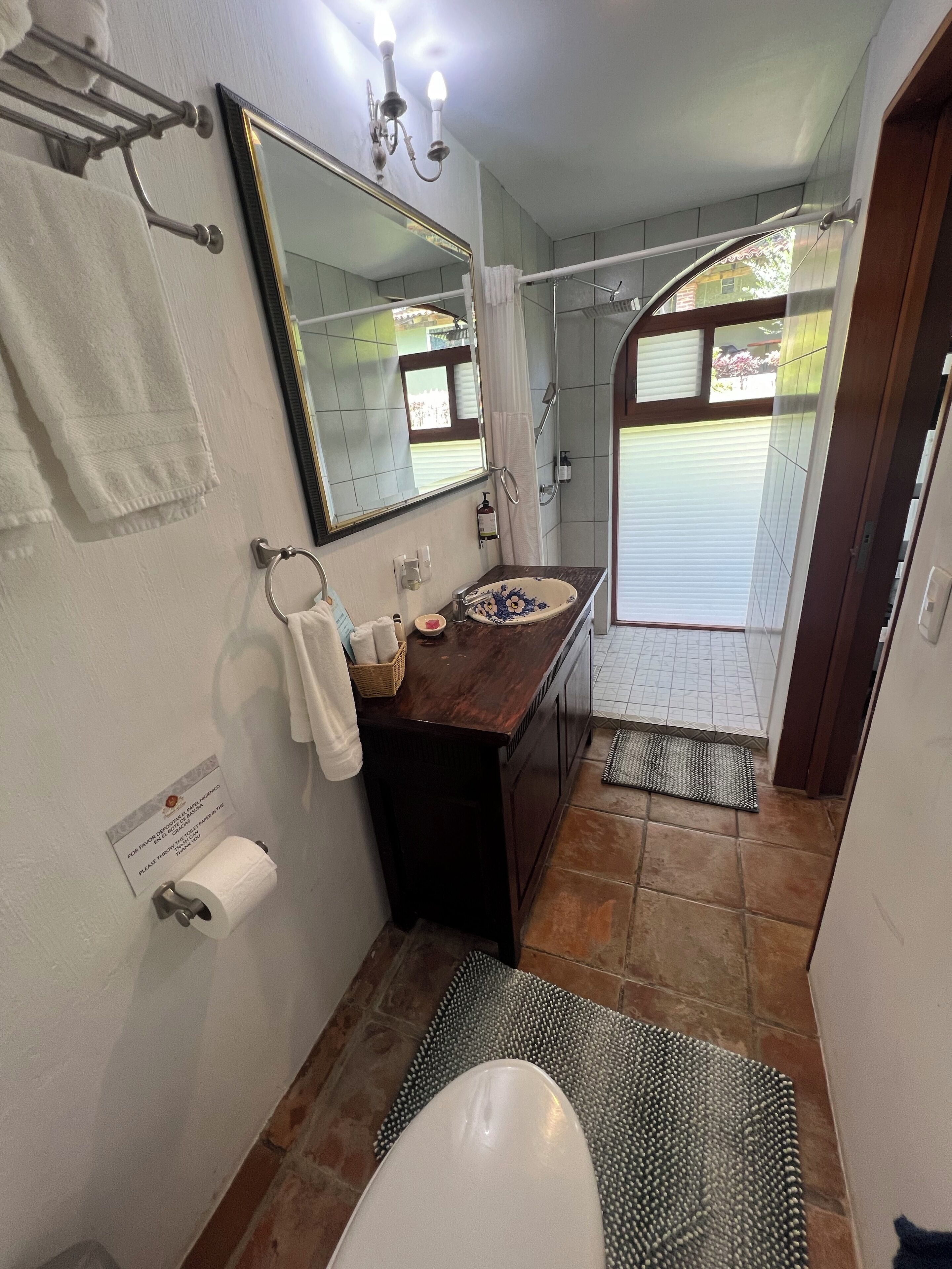 Un baño con tocador de madera, un espejo grande, toallero, inodoro y zona de ducha.