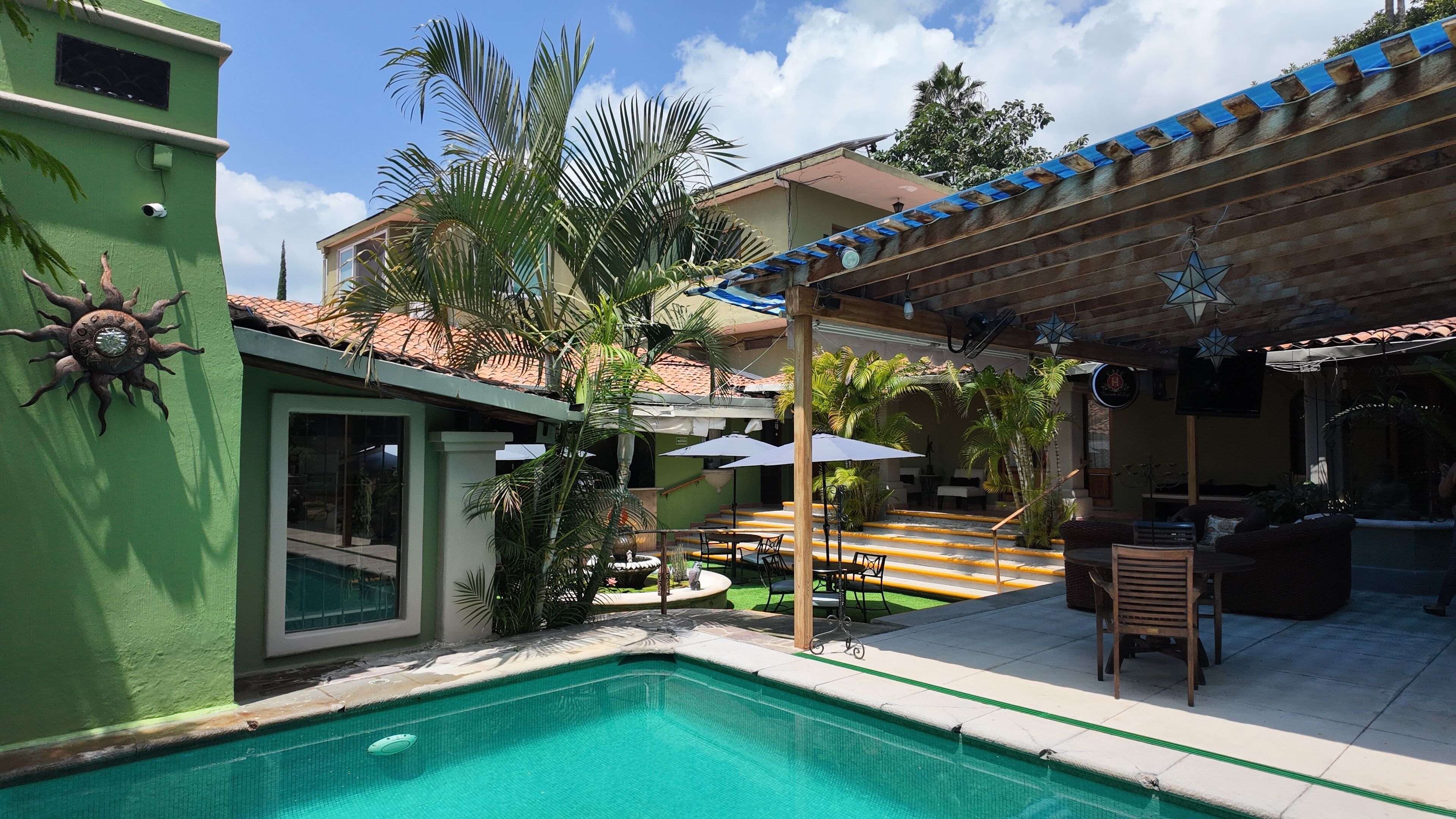 Una piscina con solárium de baldosas, mobiliario exterior y un porche cubierto.