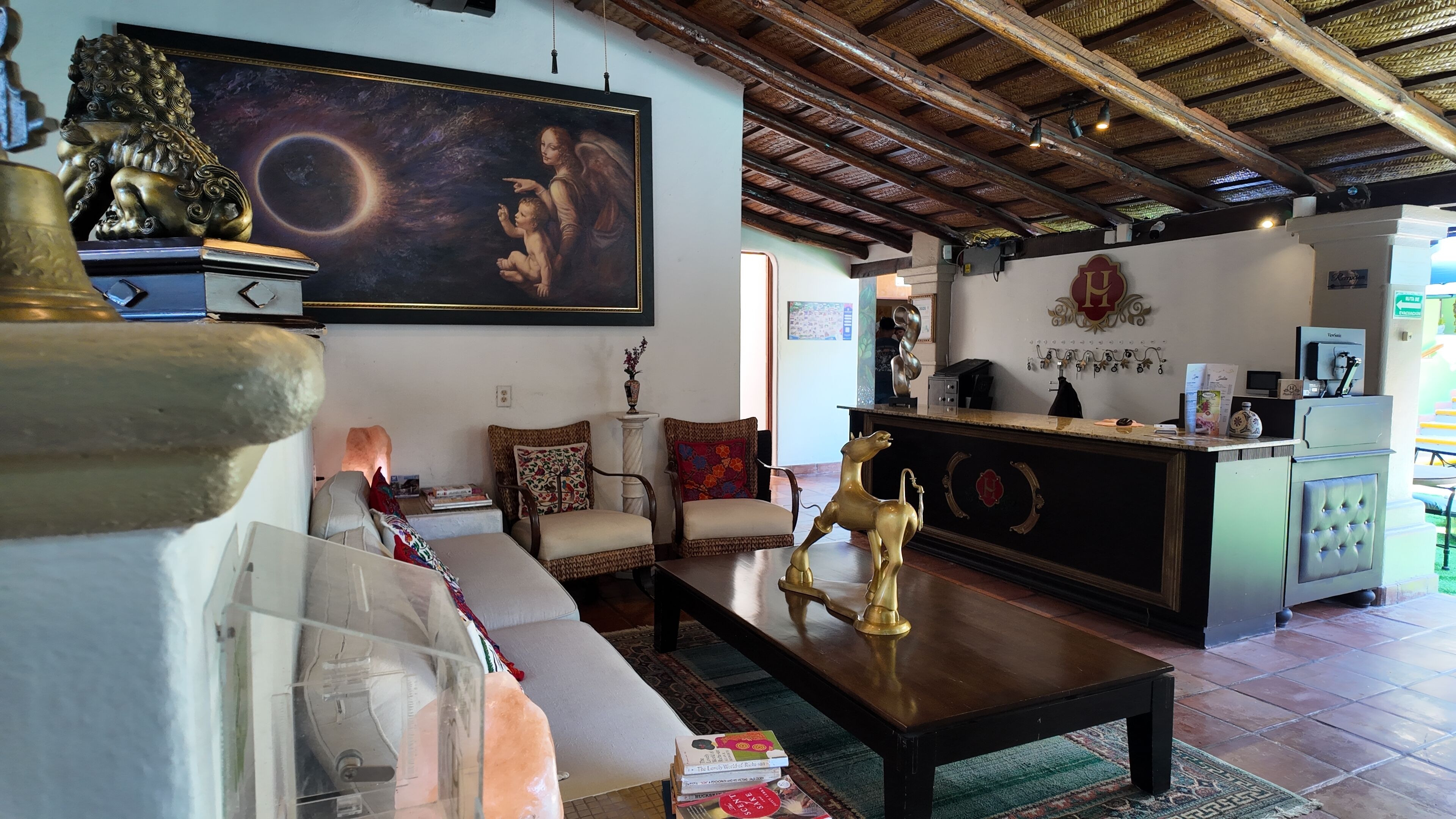 Uma sala de estar com sofá, cadeiras, mesa de centro, lareira, quadro e área de cozinha com geladeira e pia.