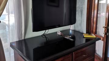Un televisor de pantalla plana montado sobre una encimera negra, armarios de madera debajo y una puerta con panel de vidrio a la derecha.