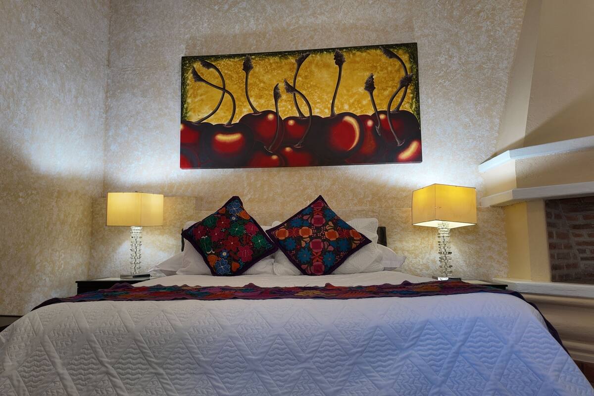 A hotel room with a bed, two lamps, a quilt, and a wall painting.