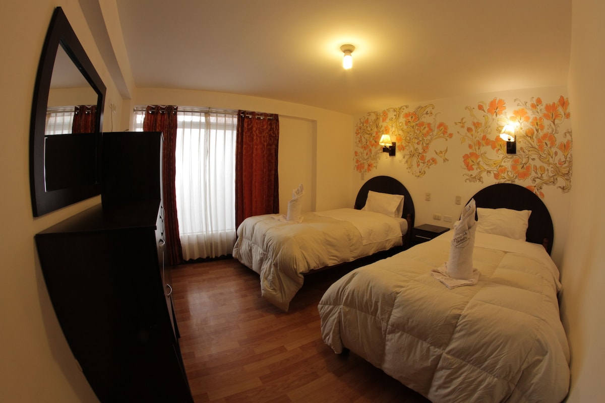A hotel room with two beds, a TV, a mirror, and a floral wall decoration.