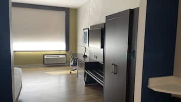 Ett hotellrum med en säng, ett skrivbord, en stol, en tv och en garderob.