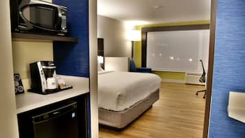 Quarto de hotel com cama, micro-ondas, cafeteira e mesa de escritório com computador.