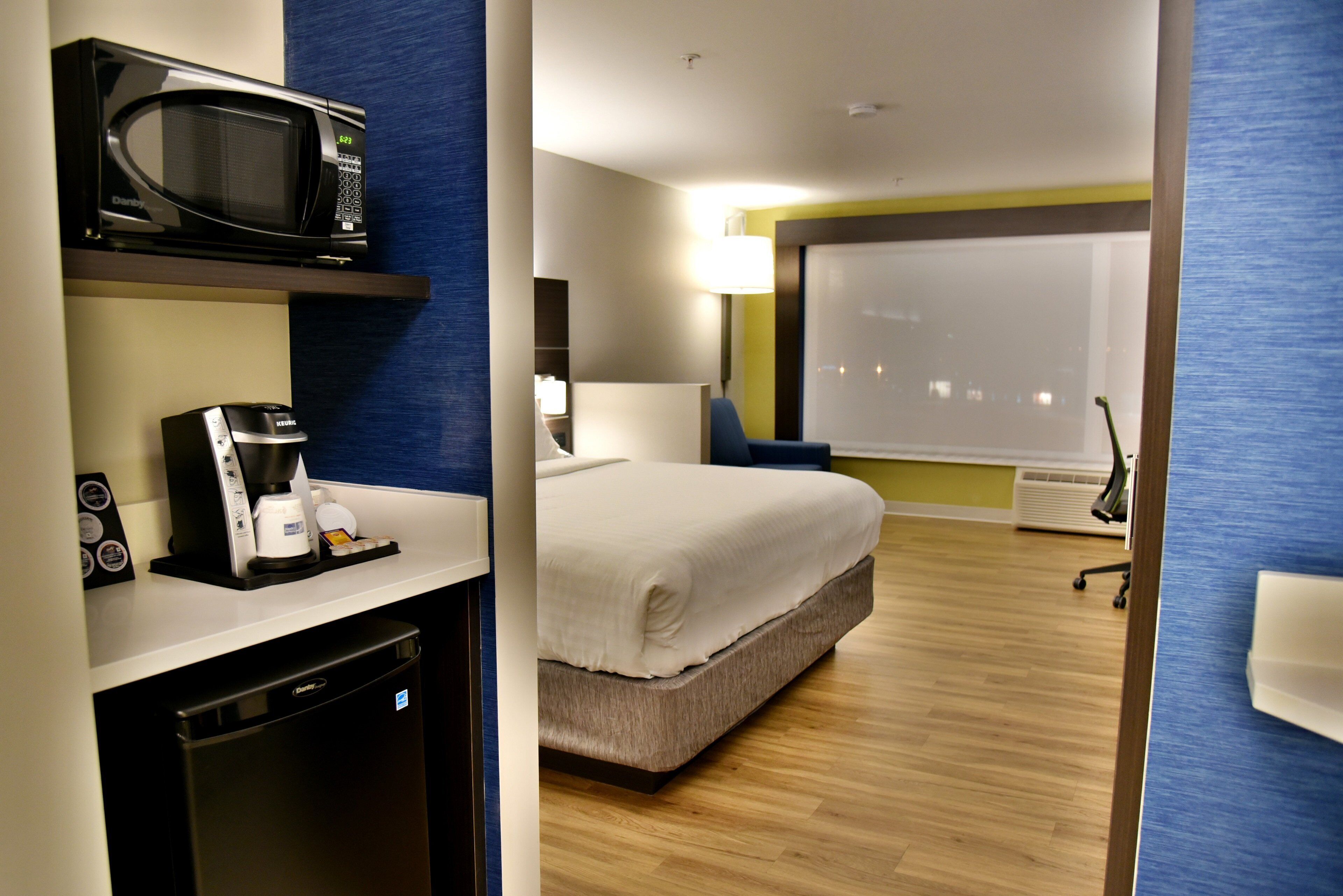 Una habitación de hotel con una cama, cafetera, microondas y escritorio con computadora.