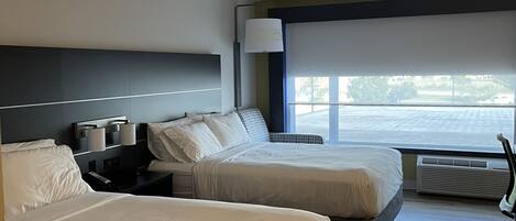 A hotel room with two beds, a desk, a chair, and a large window with a view.