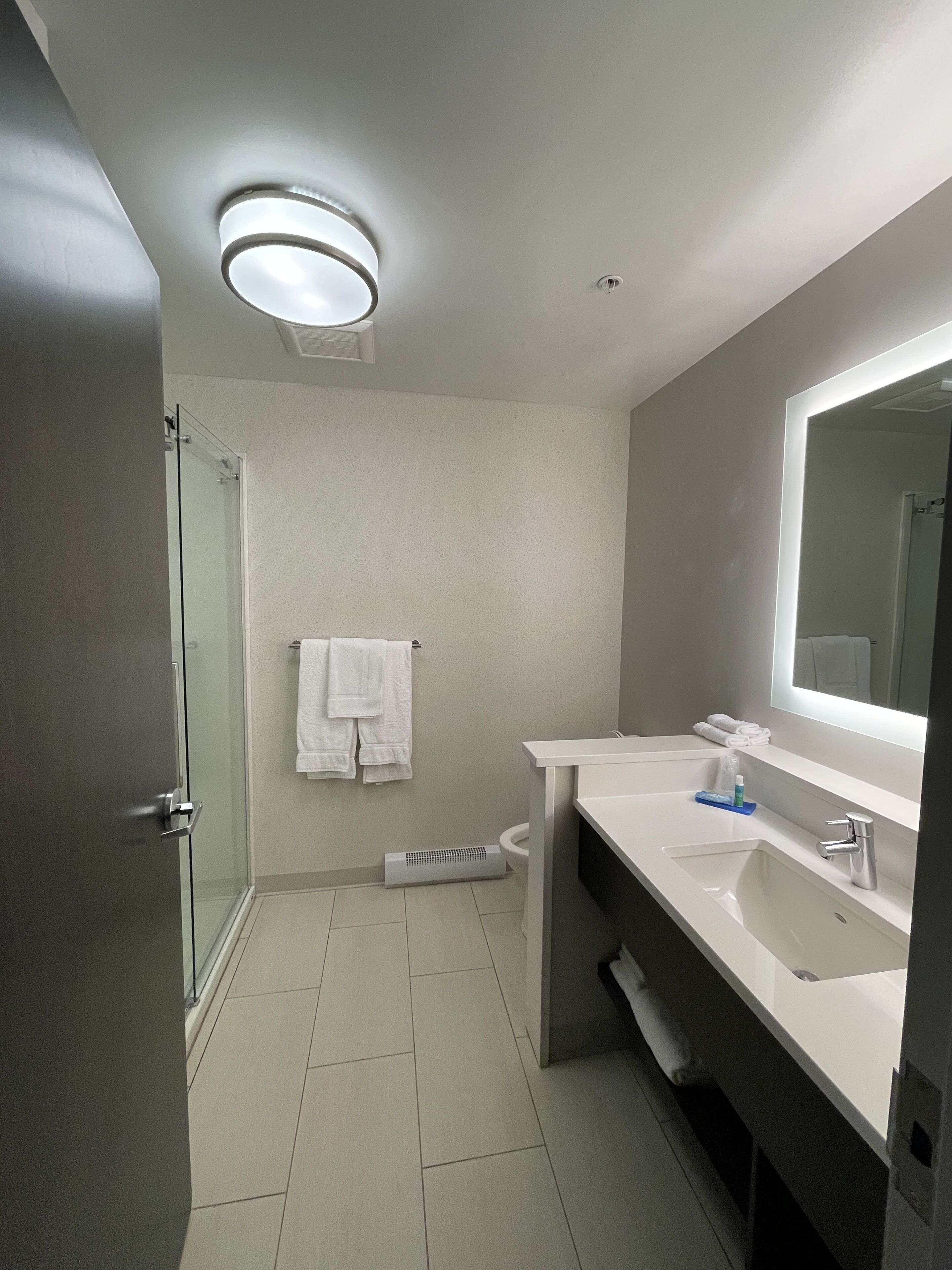 A modern bathroom with a glass shower enclosure, a white sink with a mirror, and a towel rack.