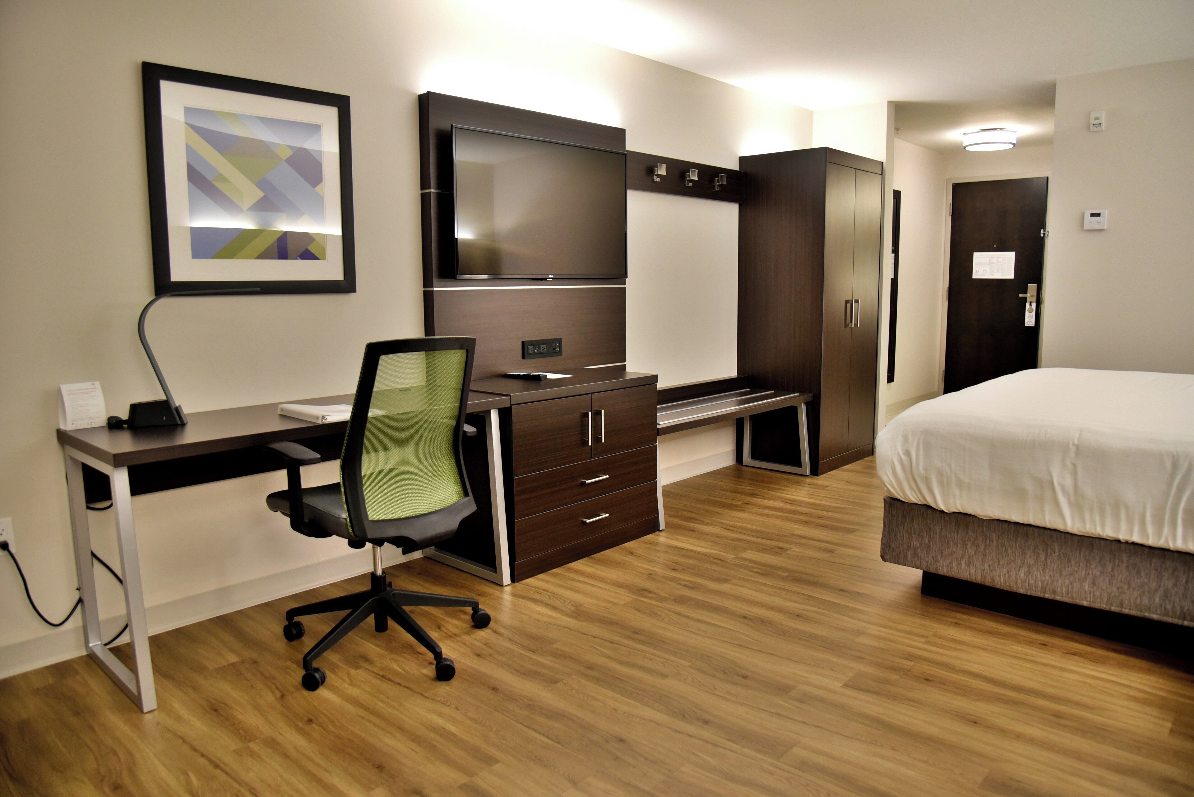 A hotel room with a bed, a desk with a chair, a wardrobe, and a television.
