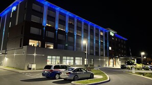 Un moderno edificio de hotel con estacionamiento, con fachada iluminada en azul y varios pisos.