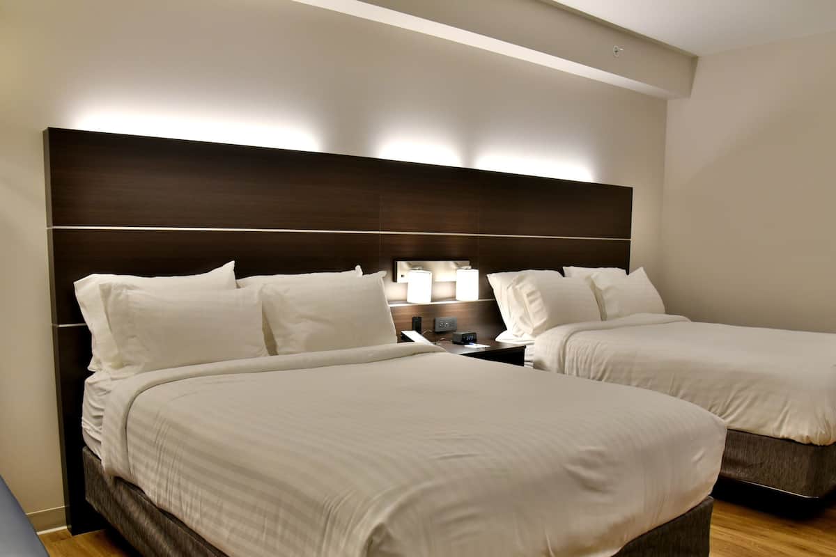 A hotel room with two beds, a nightstand, a lamp, and a wall-mounted light fixture.