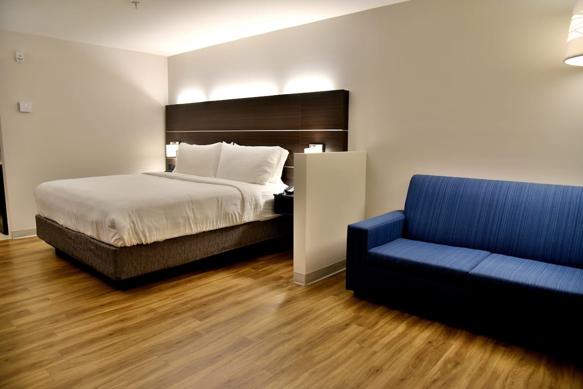 A modern hotel room with a bed, a blue sofa, and wooden flooring.