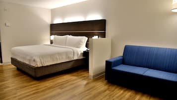 A modern hotel room with a bed, a blue sofa, and wooden flooring.