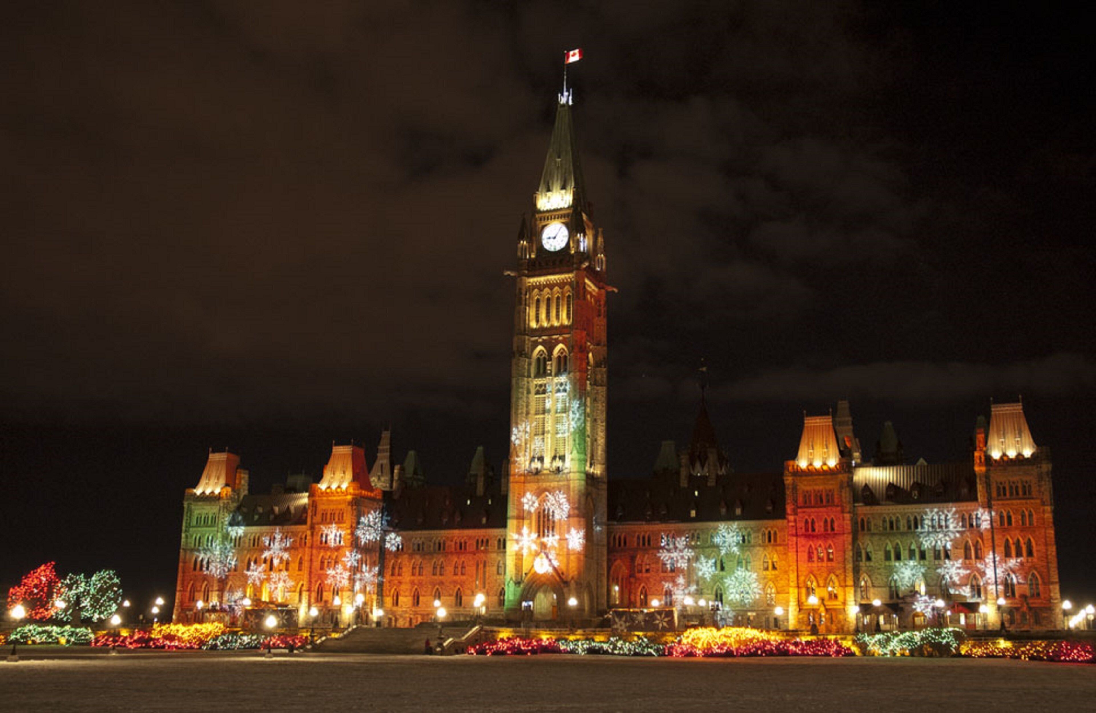 A large building with a prominent clock tower, illuminated by colorful lights.
