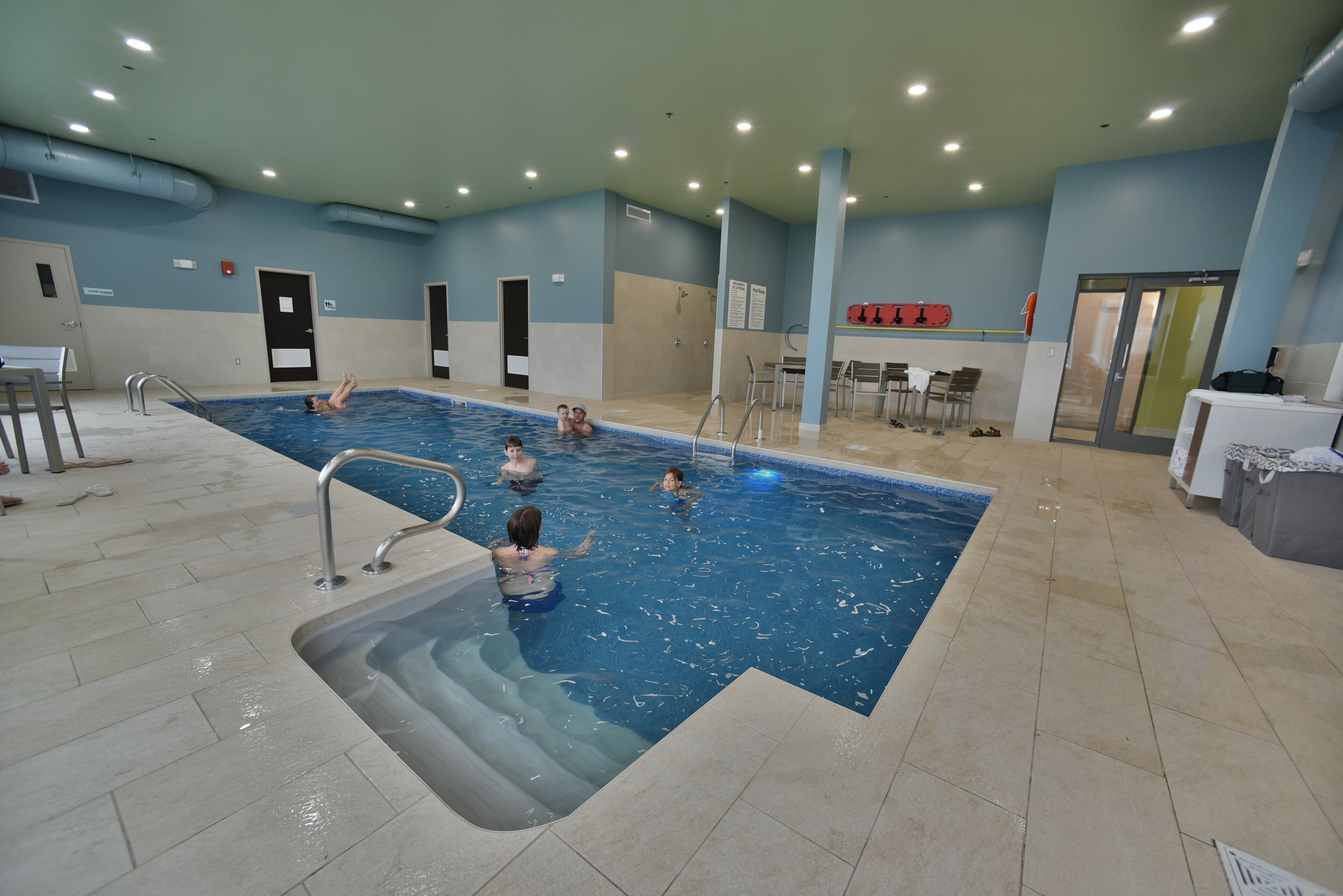 An indoor swimming pool with multiple lanes, safety railings, and a changing room area.