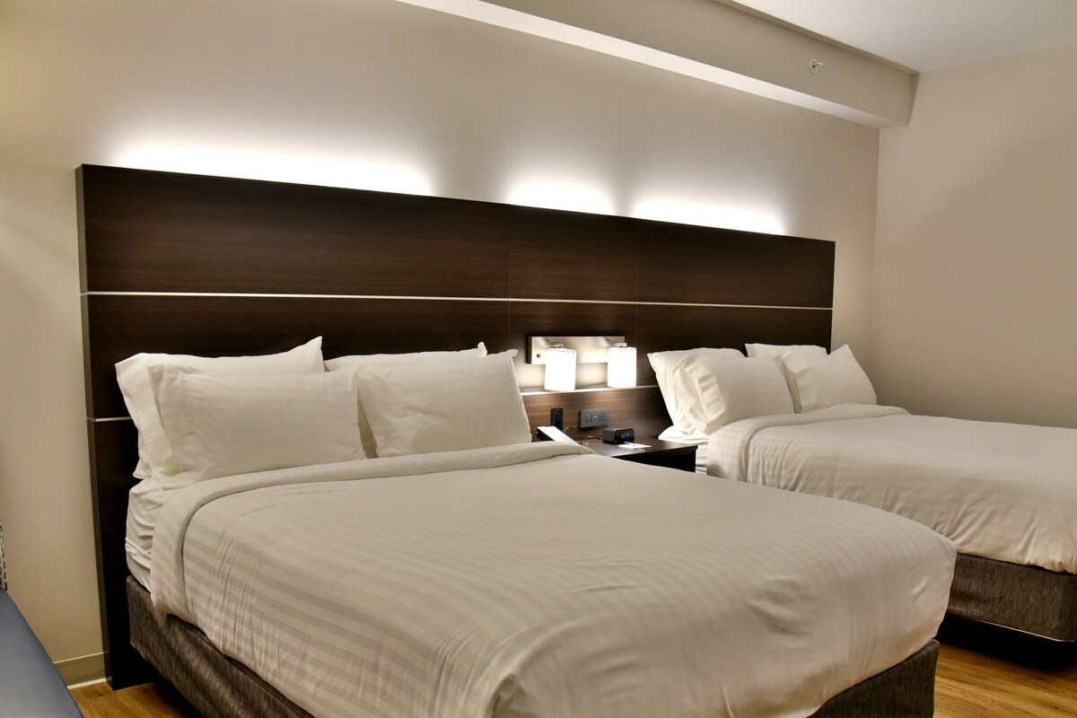 Habitación de hotel con dos camas, una mesita de noche, una lámpara y una lámpara de pared.